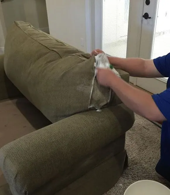 Person cleaning a green couch cushion with a cloth in a living room