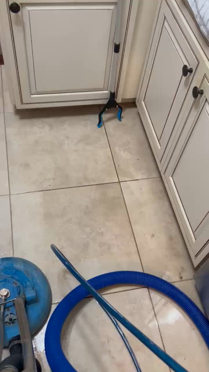 Blue cleaning equipment on a beige tiled floor beside white cabinets.