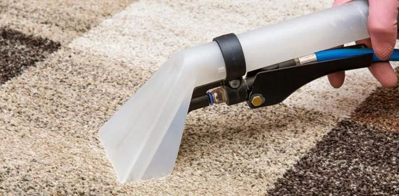 Close-up of a spray nozzle cleaning a beige carpet, releasing a white cleaning solution.