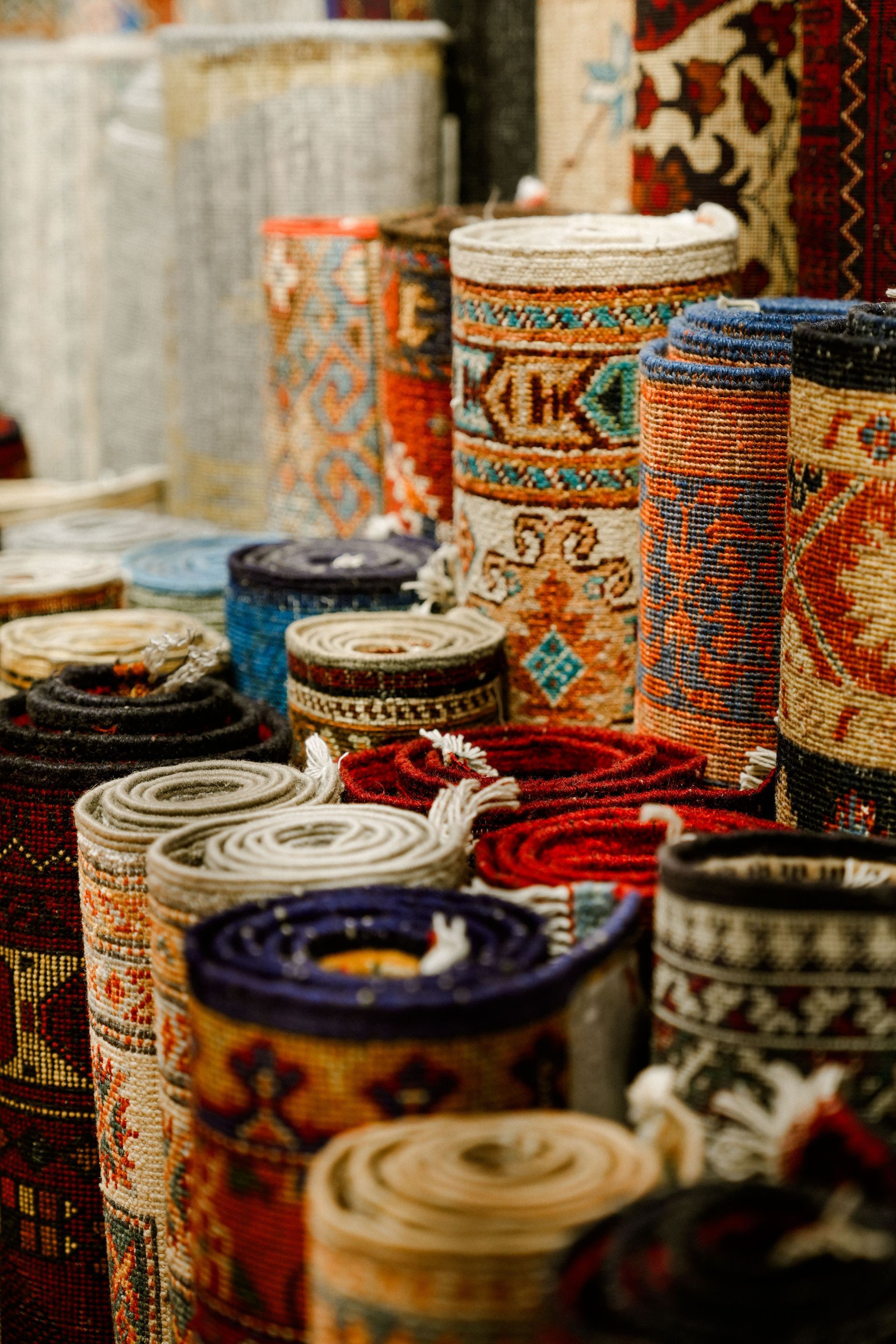 Colorful rolled woven rugs and mats stacked together in a market stall.