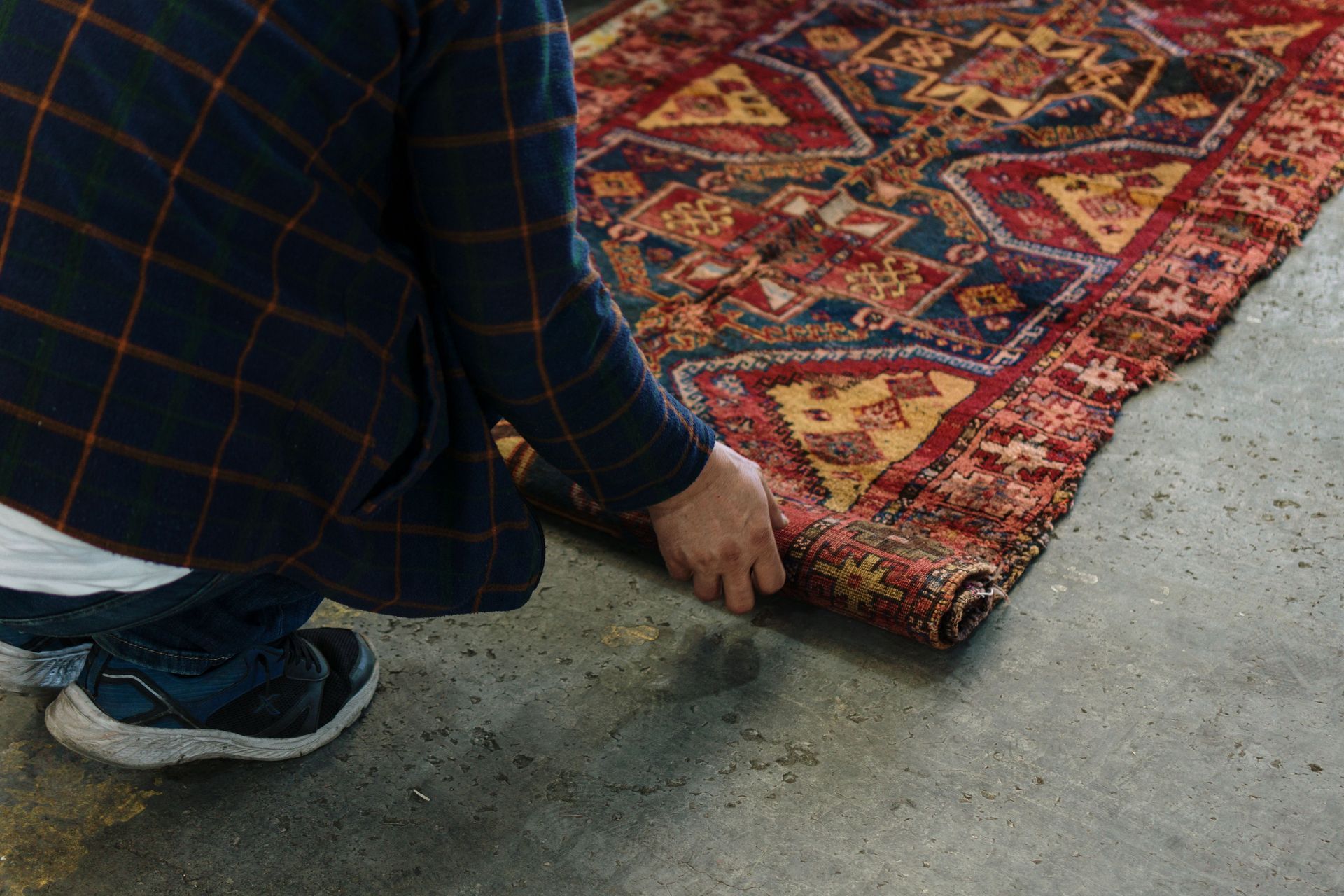 Person kneeling to straighten a red patterned rug on a concrete floor