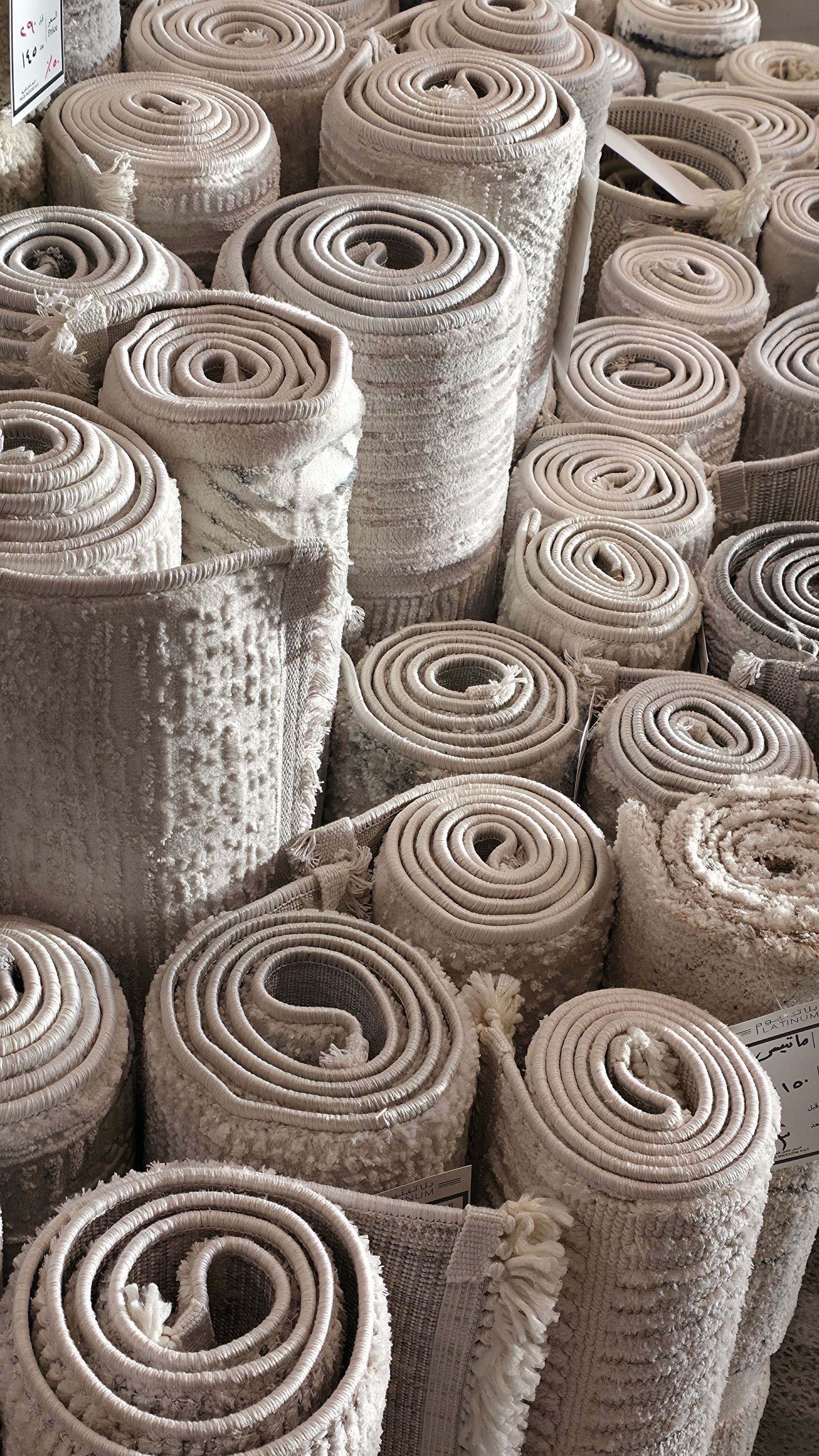 Stacked rolled beige woven mats or rugs filling the frame in a store or warehouse