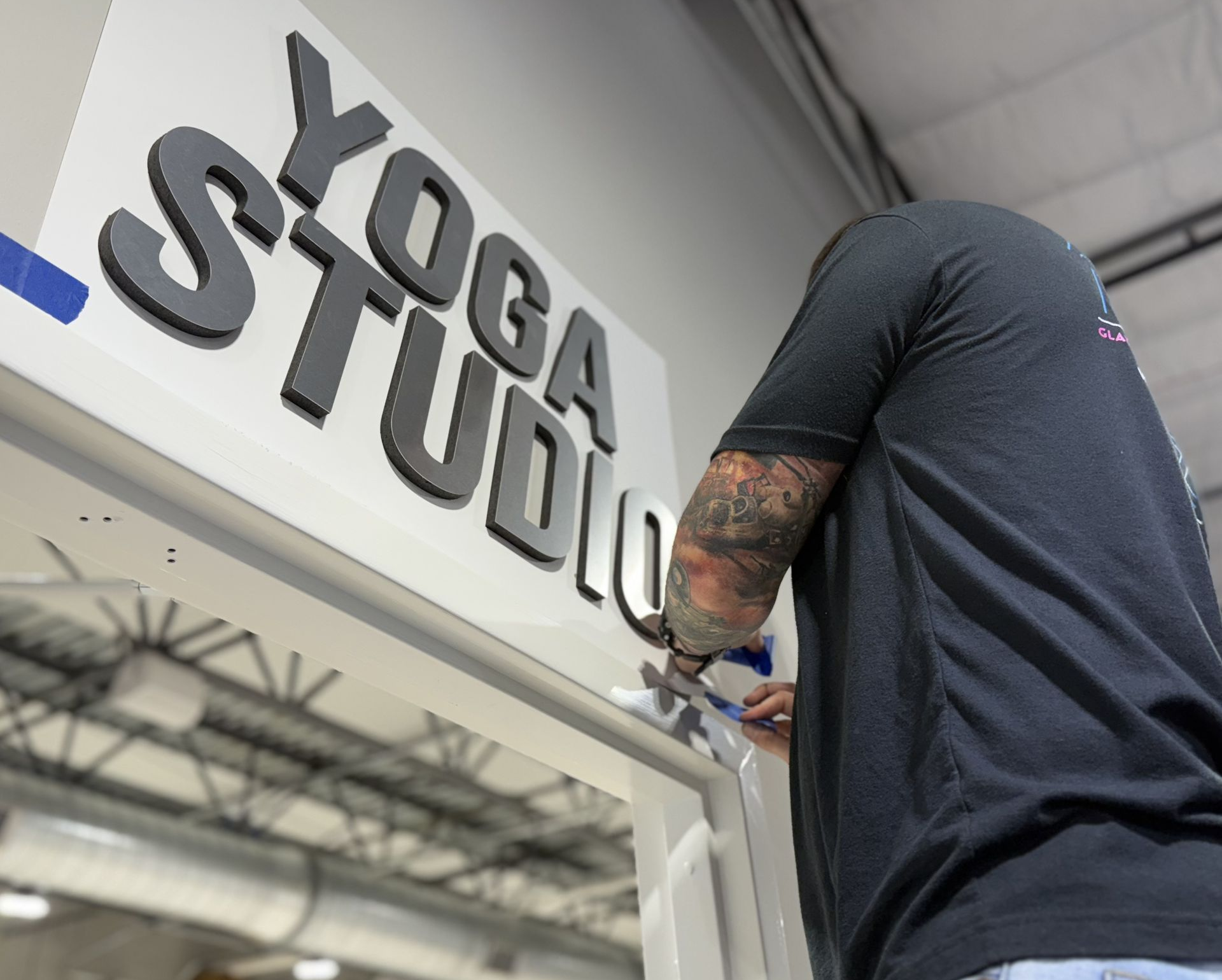 Person installing a sign reading “YOGA STUDIO” above a doorway inside a building.