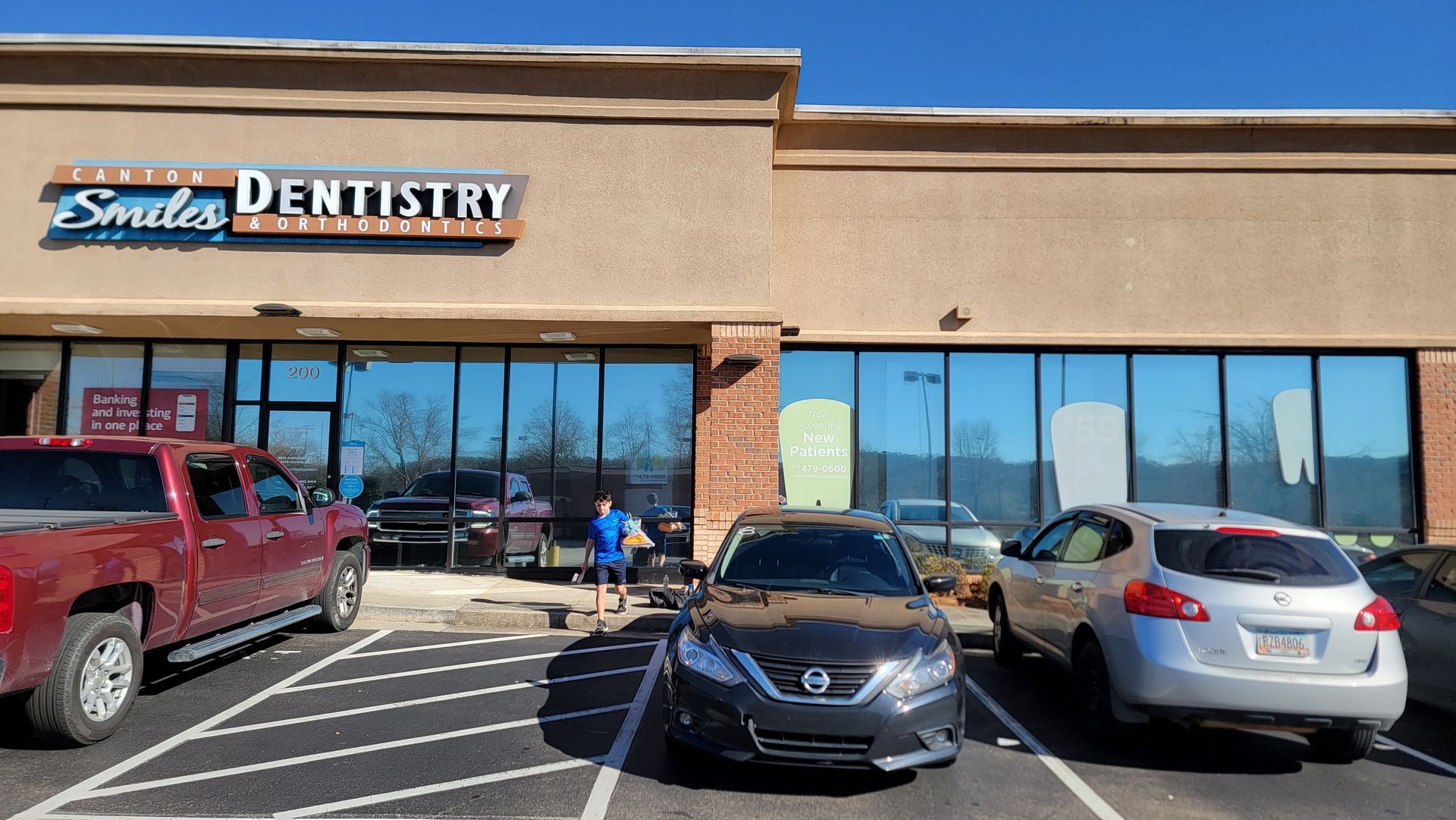 Strip mall storefront for Smile Dentistry with parked cars and a person walking toward the entrance