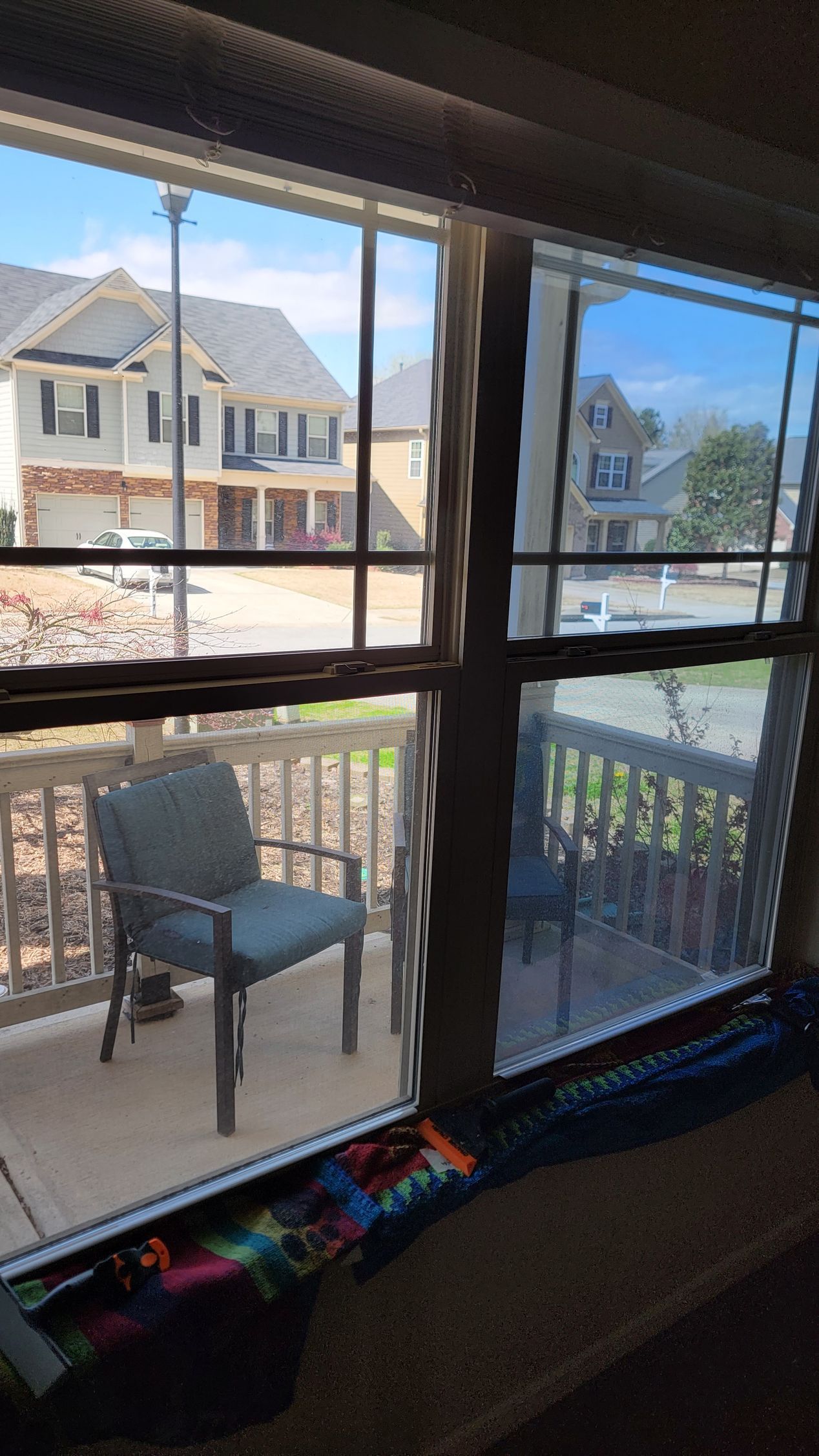 View through a window to a porch chair and suburban houses across the street under a blue sky