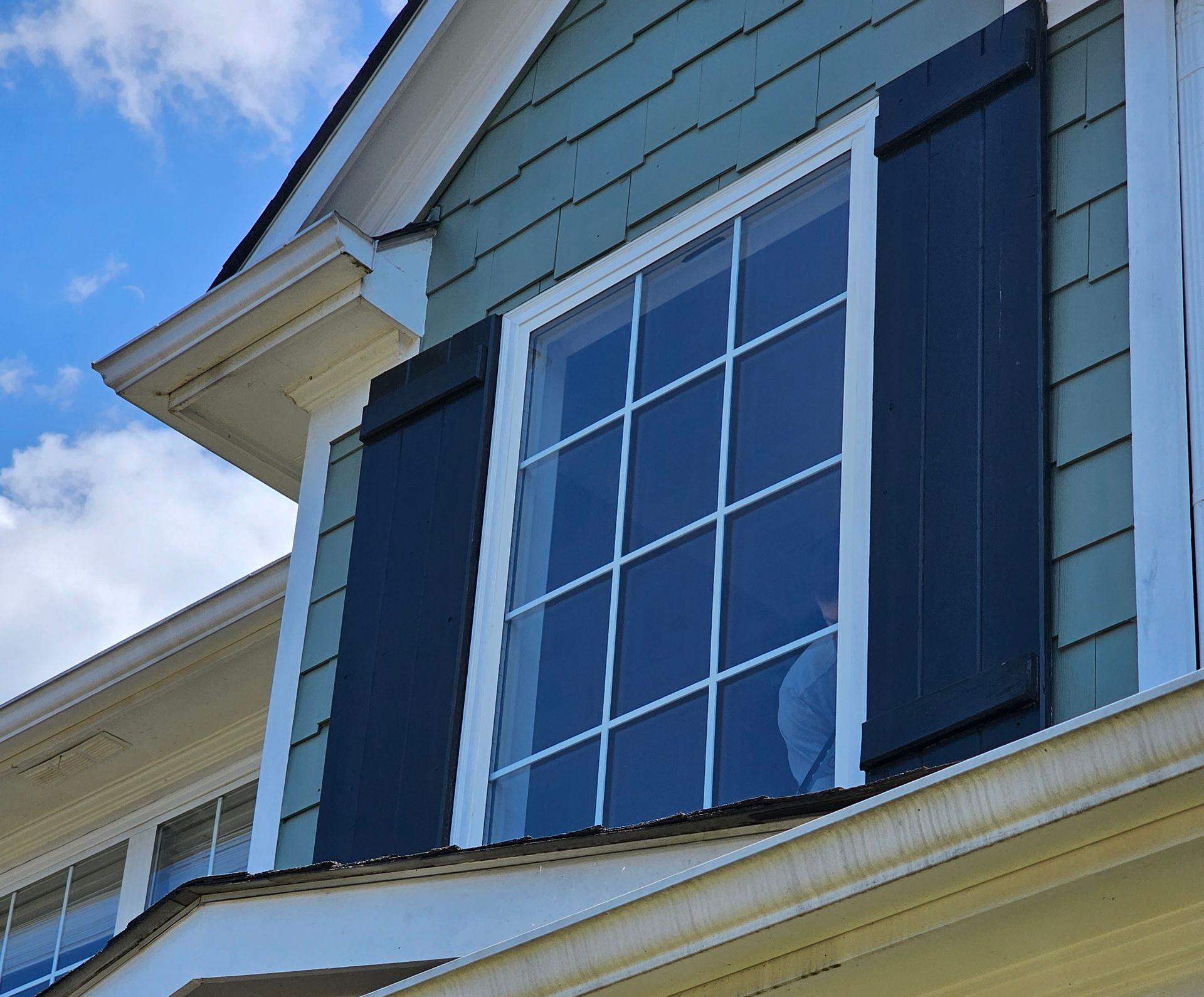 Blue shutters framing a white-trimmed window on a light green house exterior under a blue sky
