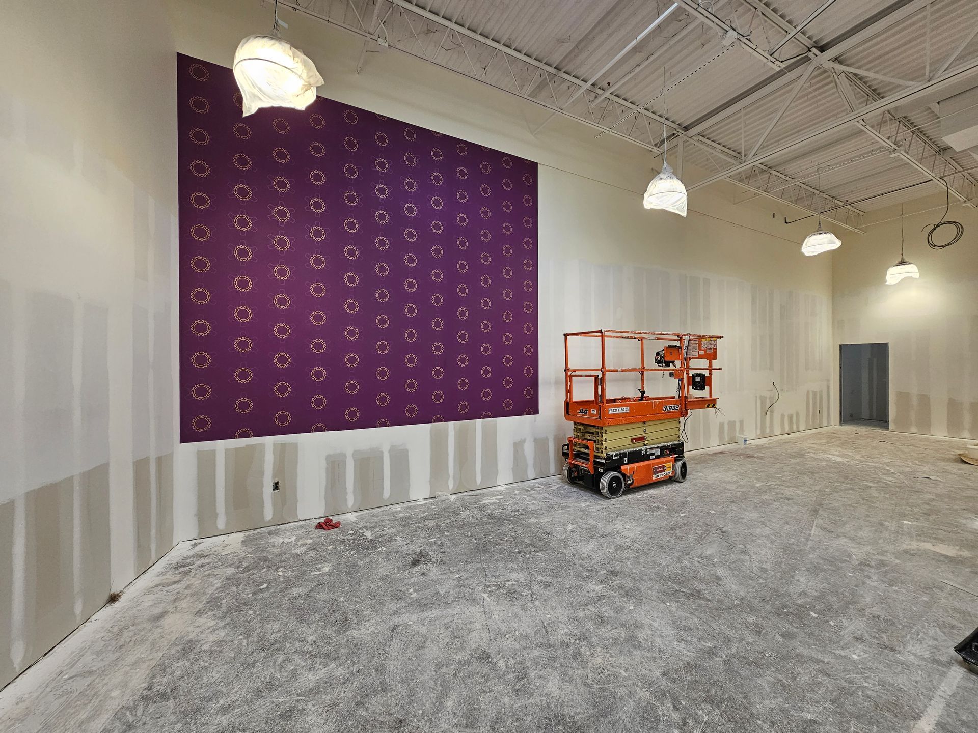 Construction site with purple accent wall, orange lift, and unfinished white room under hanging lights