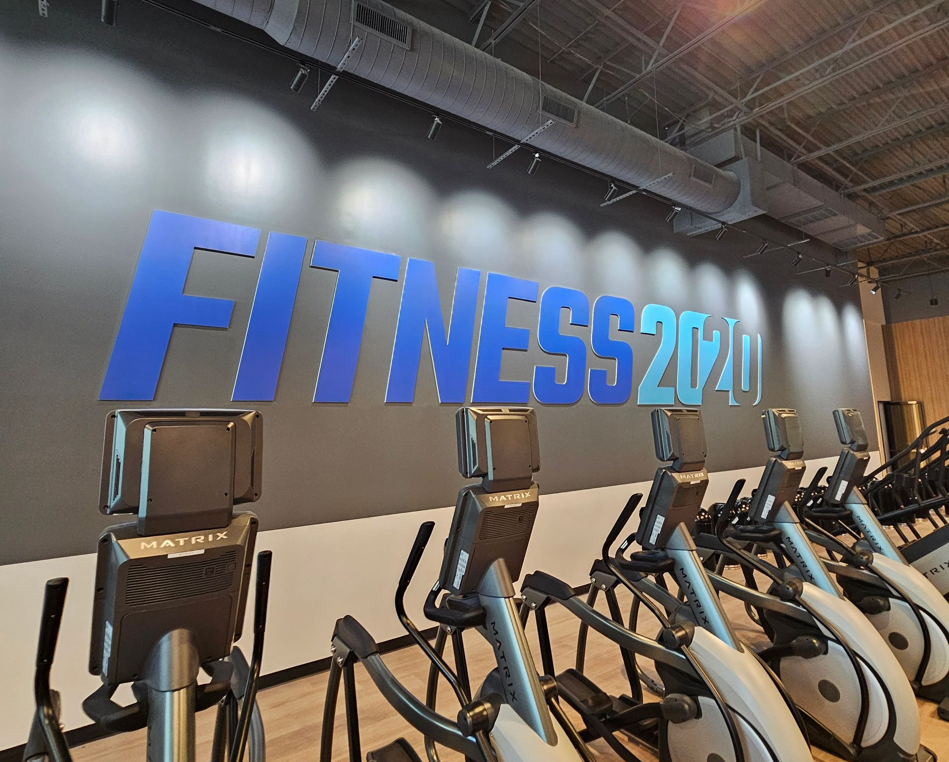 Row of exercise bikes in a gym with a large blue “FITNESS 24/7” wall sign
