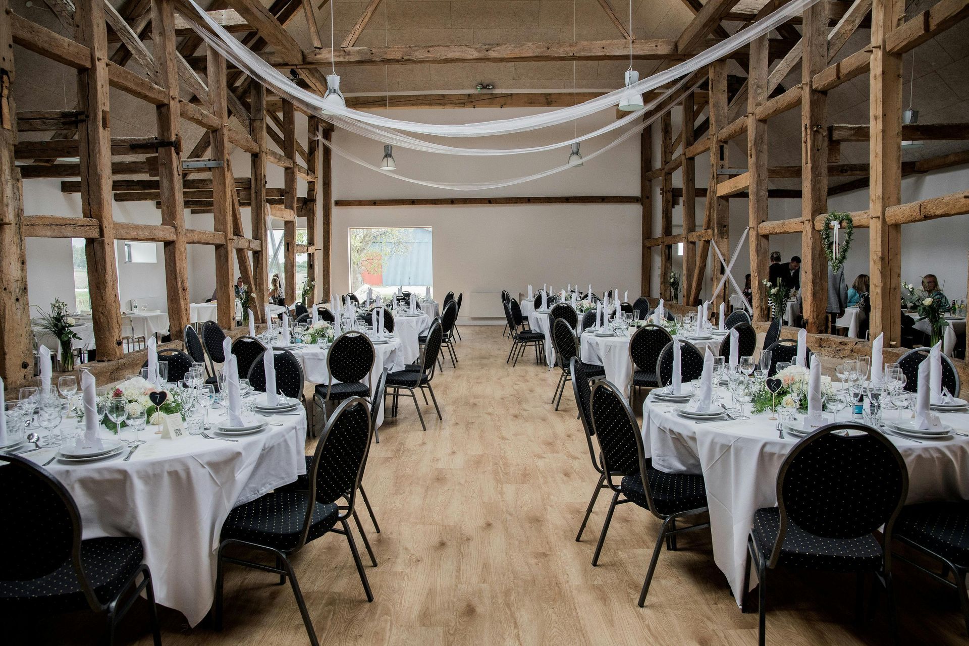 Elegant dining room set for a celebration. Round tables with white linens, gold chairs, and floral centerpieces.