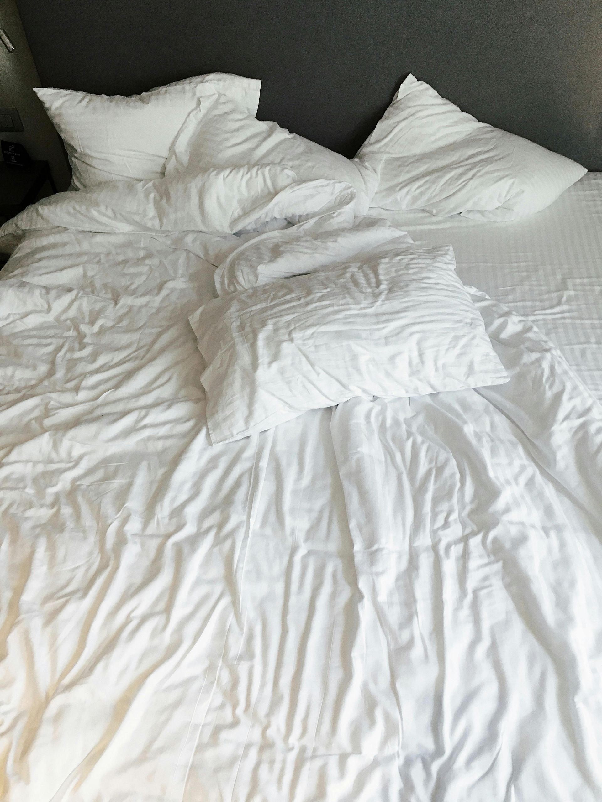 Wrinkled white bedding with three pillows on a bed.