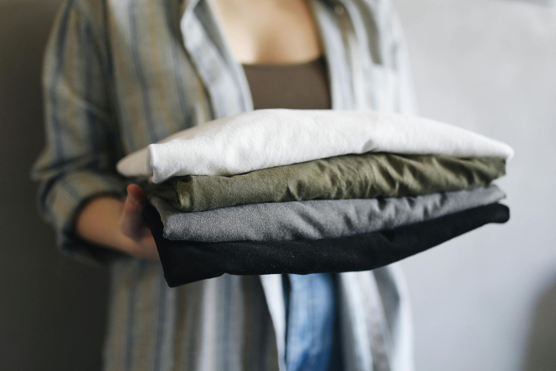 Woman holding a stack of neatly folded shirts in various colors against a gray backdrop.
