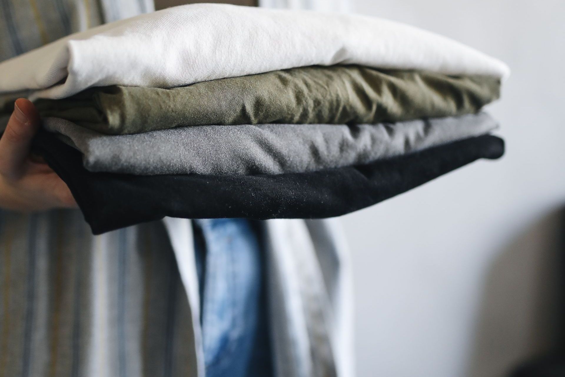 Person holding a stack of four folded t-shirts: white, green, gray, and black.