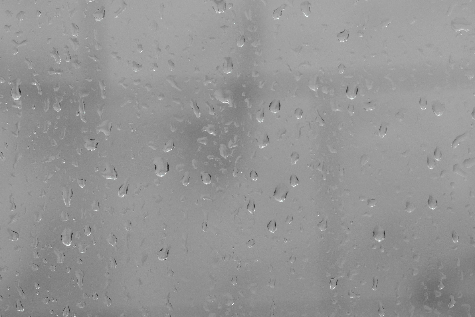 Raindrops on a window with a blurry gray outdoor scene beyond