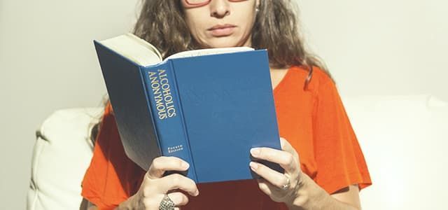 Person in orange shirt reading a blue book on a couch