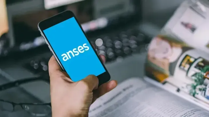 Una persona sostiene un teléfono celular con la palabra anses en la pantalla.