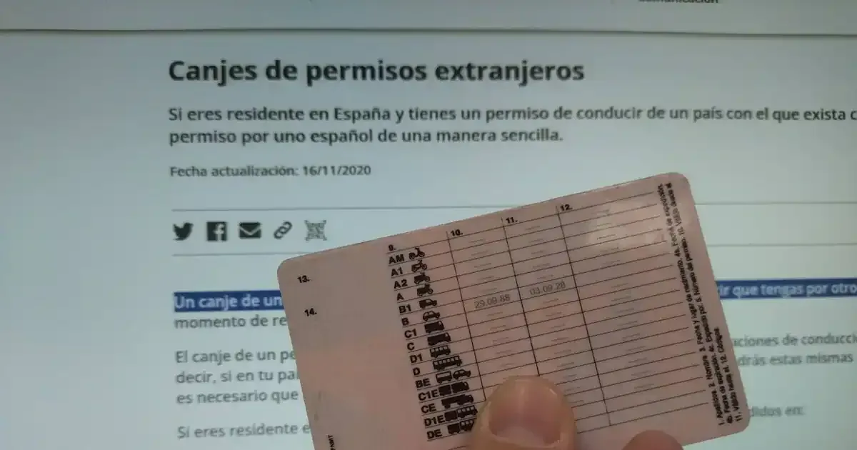 Una persona sostiene un permiso de conducir español delante de una pantalla de ordenador.