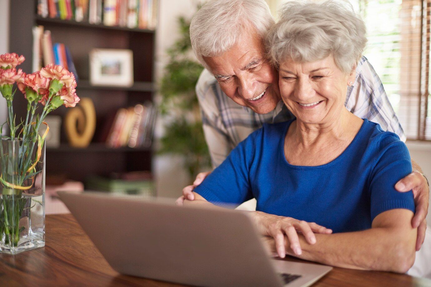 Una pareja de ancianos está sentada en una mesa mirando una computadora portátil.