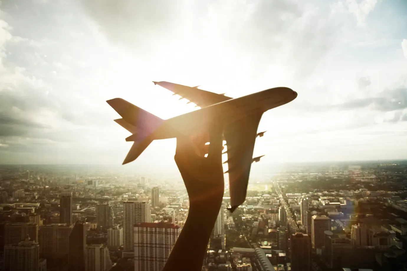 Una persona sostiene un avión en su mano sobre una ciudad.