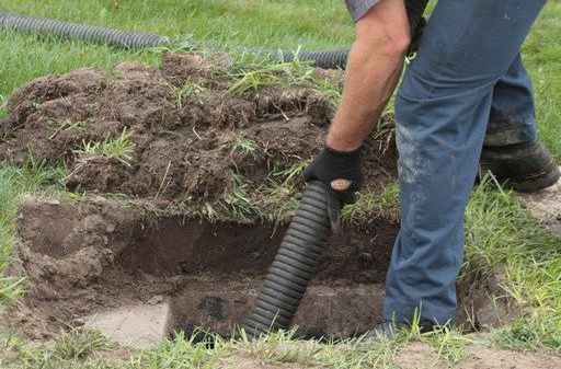 A man is using a vacuum hose to clean a a septic tank in the ground.