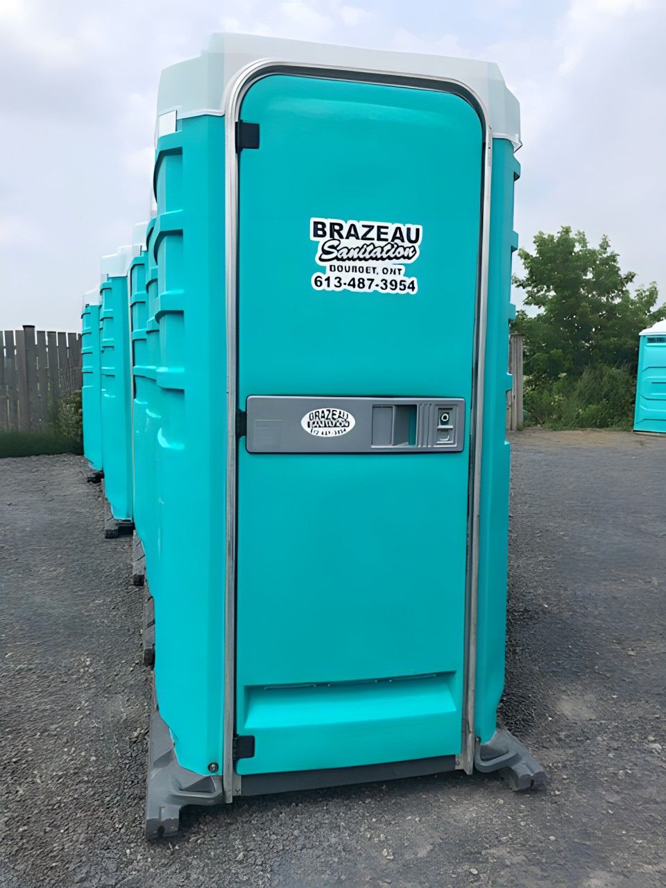A row of blue portable toilets are lined up in a parking lot. Brazeau Sanitation