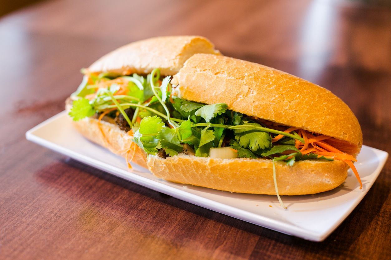 A sandwich is sitting on a white plate on a wooden table.