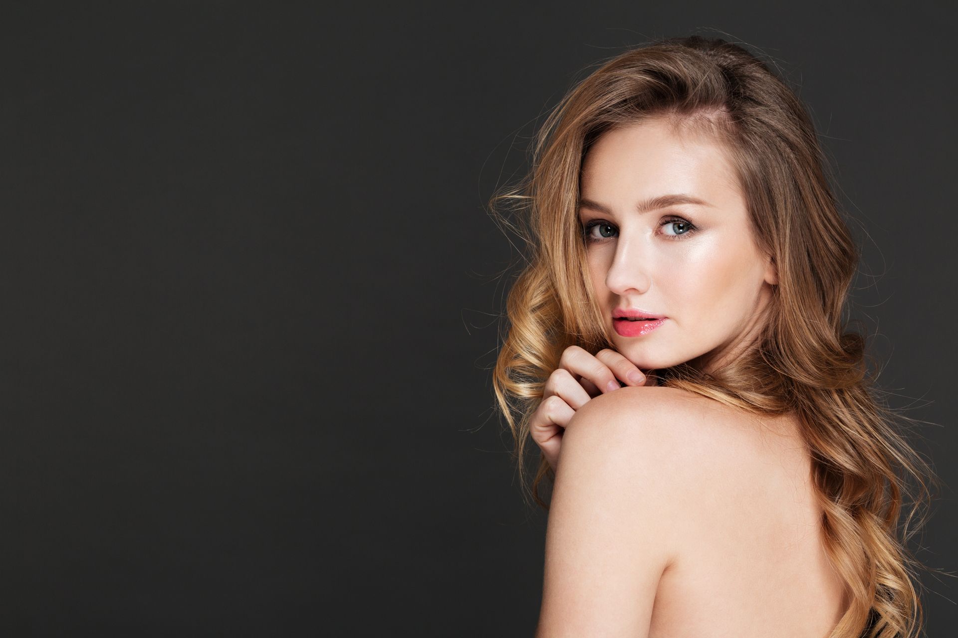 A woman without a shirt is looking over her shoulder at the camera.