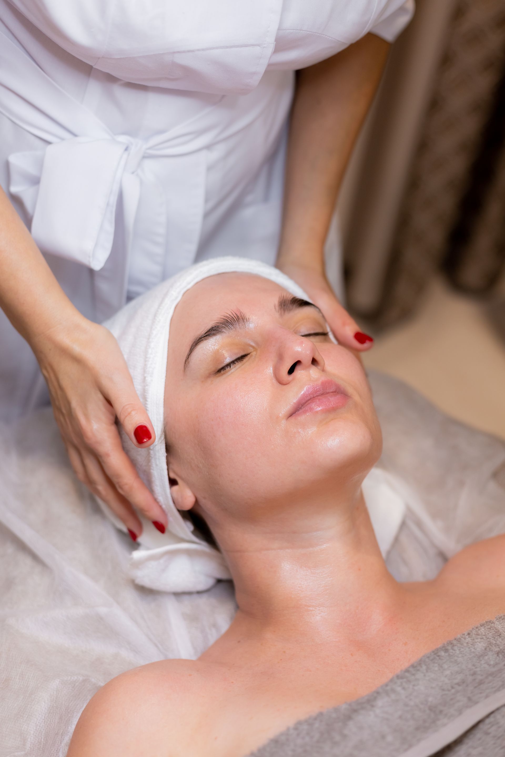 Person receiving a facial massage at a spa. Hands on face, eyes closed. White cloth wrap and robe.