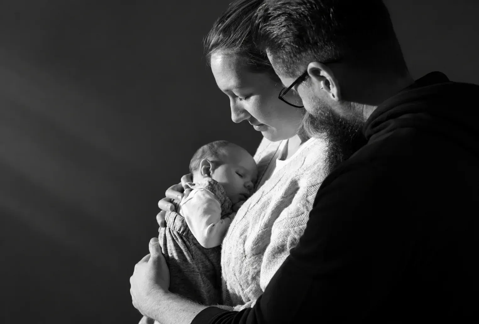 Natürliches Familienporträt mit Baby in Schwarz-Weiß Eltern betrachten ihr schlafendes Baby in einem Schwarz-Weiß-Porträt
