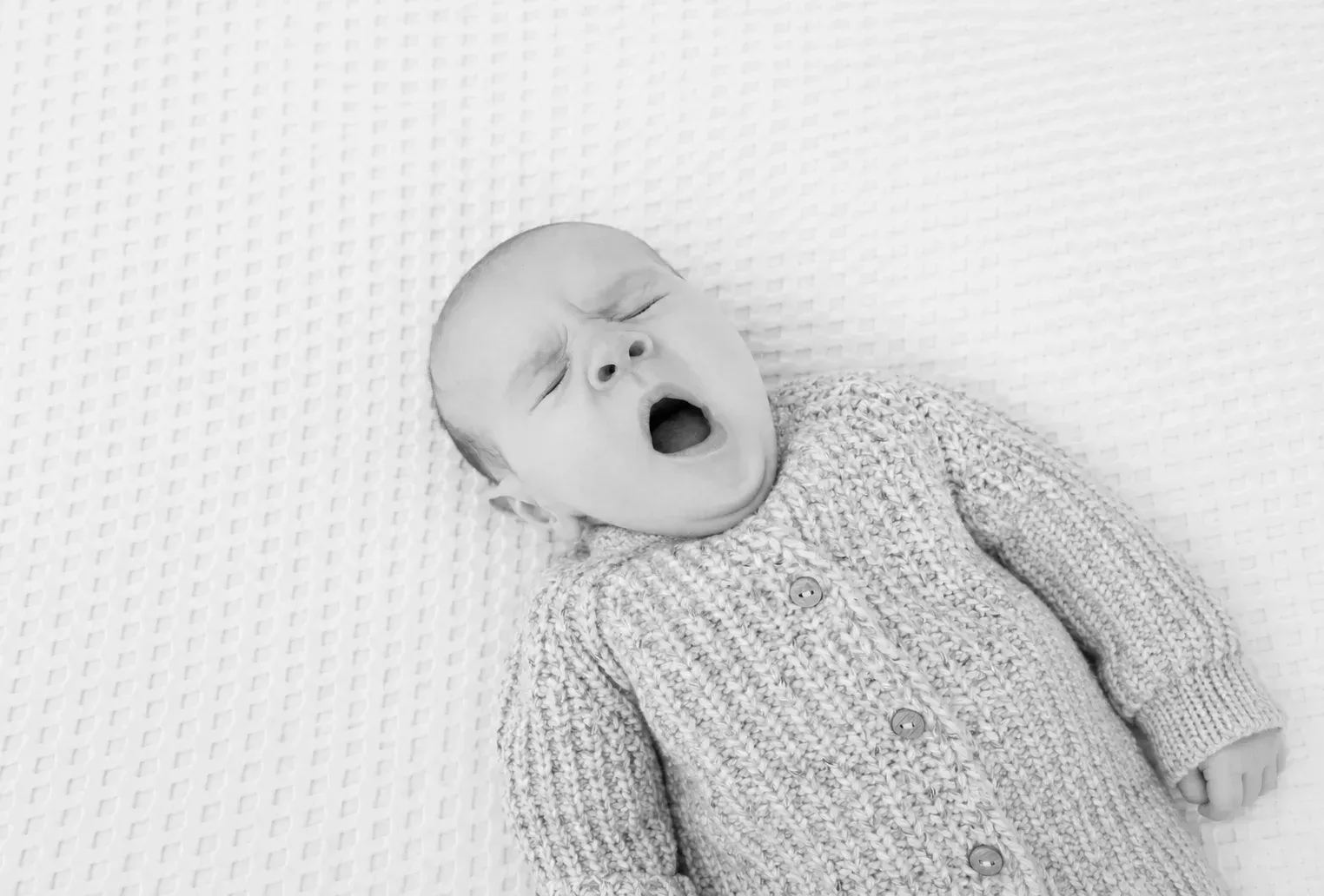 Natürliches Babyporträt eines gähnenden Babys Gähnendes Baby im Strickjäckchen in Schwarz-Weiß