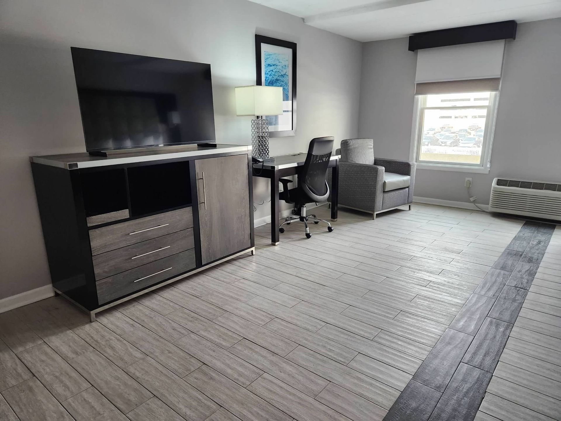 A hotel room with a desk , chair , television , and dresser.