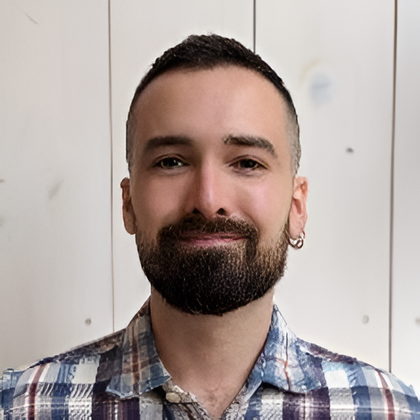 Retrato de un hombre sonriente con barba corta, vestido con una camisa azul de cuadros sobre un fondo claro
