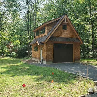 A small wooden garage with a roof that is surrounded by trees.