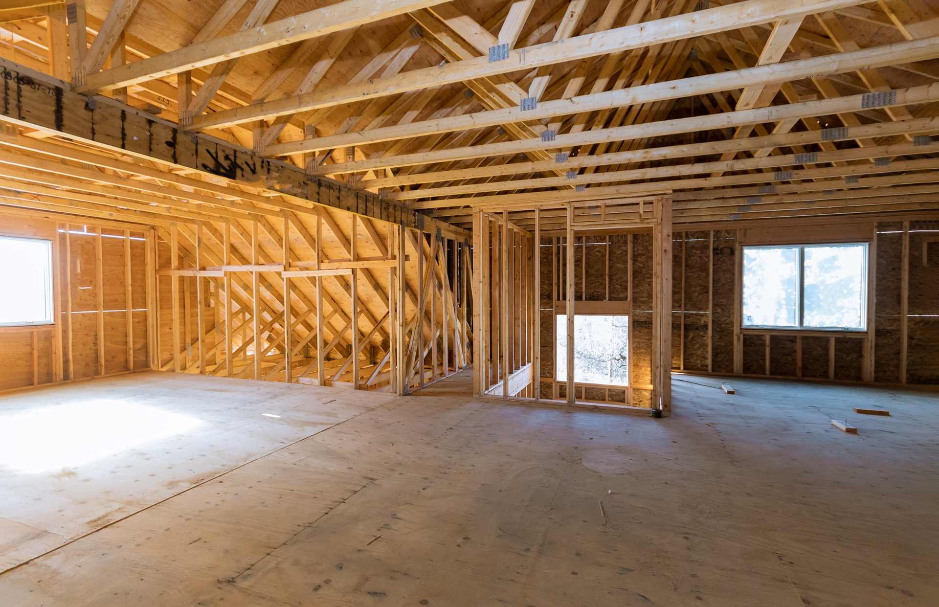 An empty room in a house under construction with wooden beams and windows.