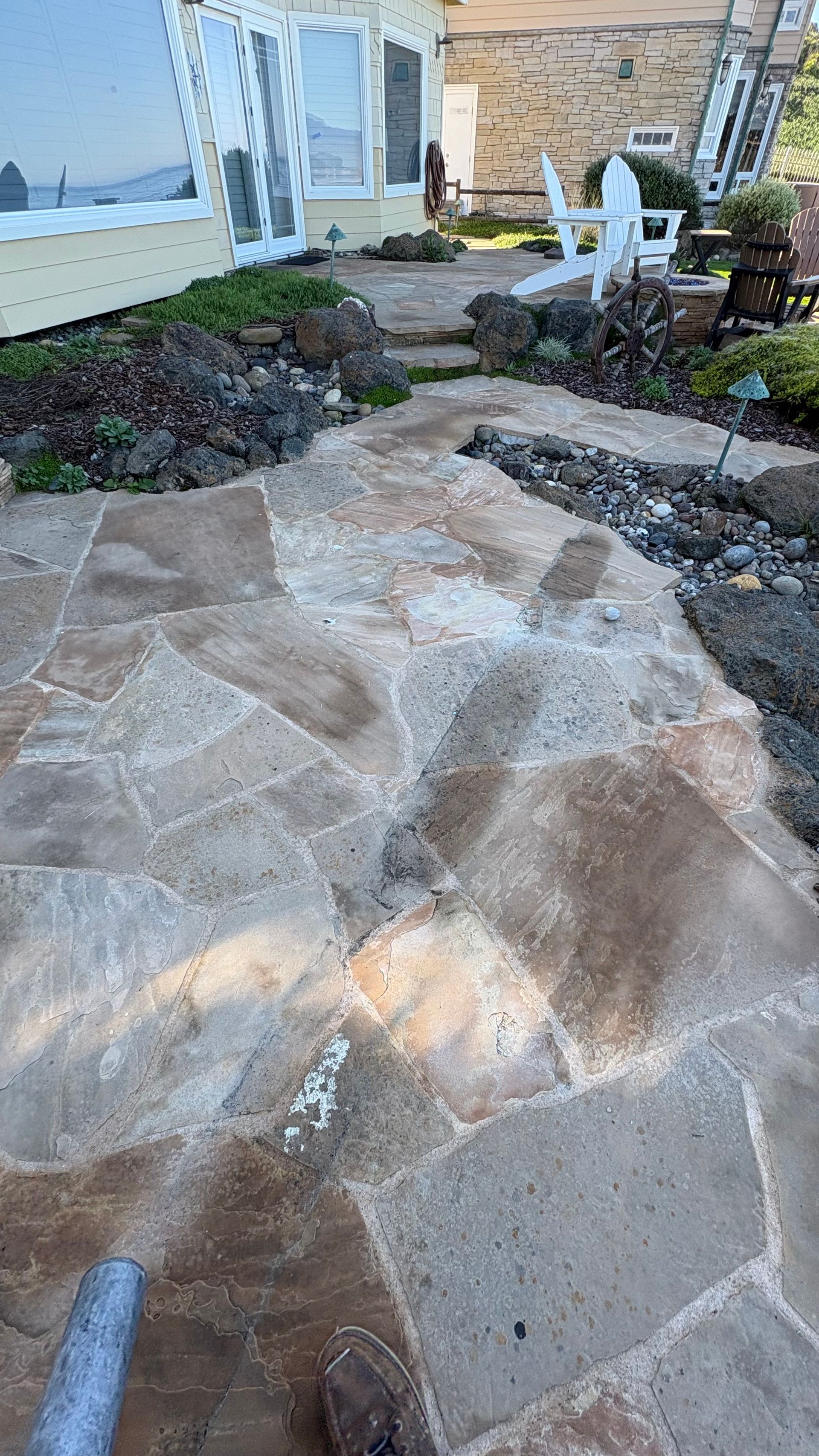 A close-up view of a power washer cleaning a stone patio, showing a streak of clean stone against dirtier sections.