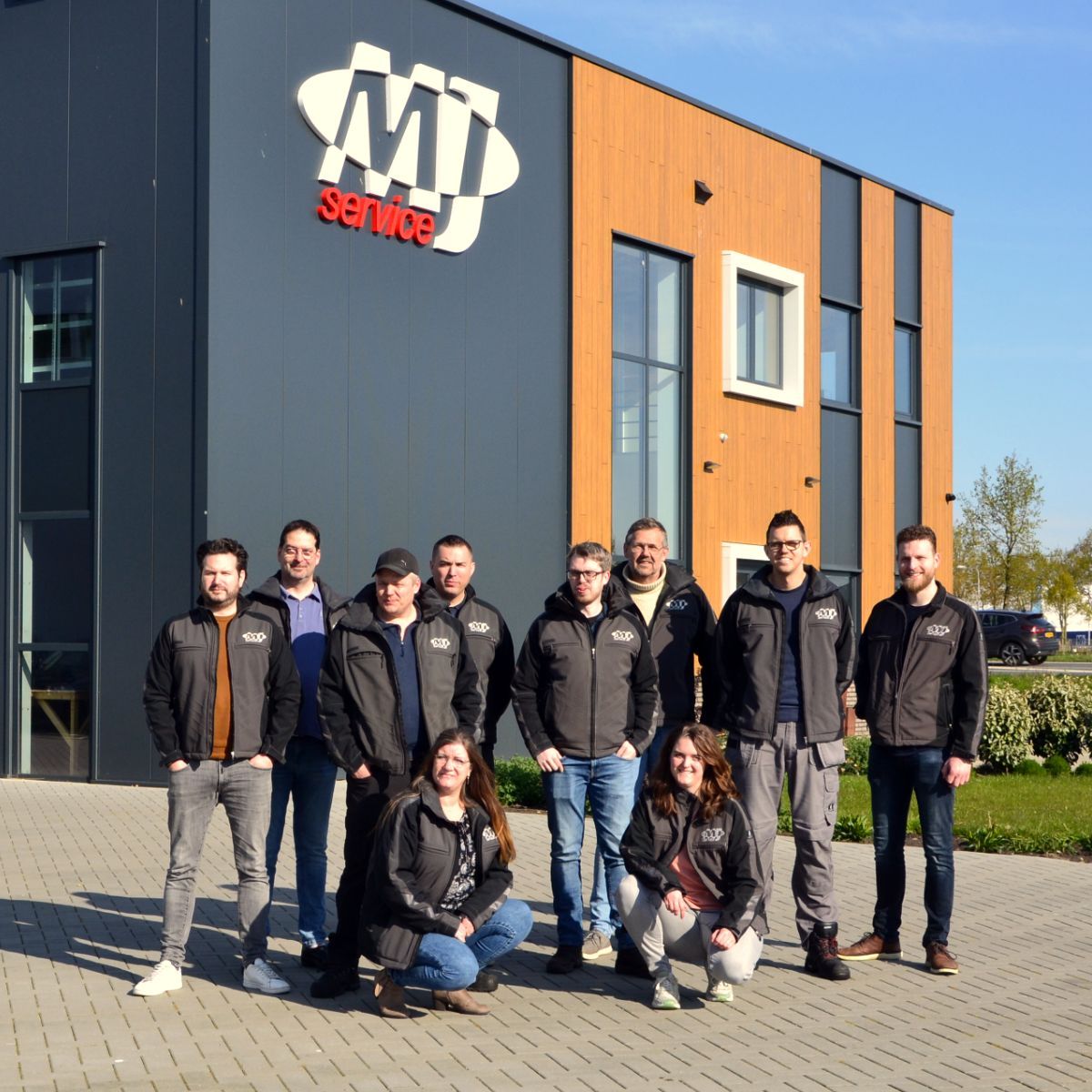 Een groep mensen poseert voor een gebouw met de tekst Ohaus MJservice