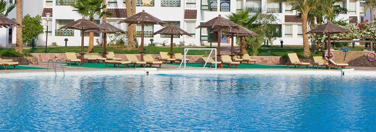 A large swimming pool surrounded by chairs and umbrellas in front of a hotel.