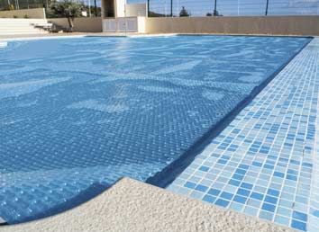 A large swimming pool covered in blue tiles and a blue cover.