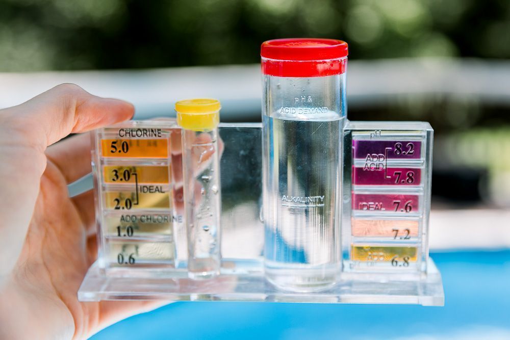 A person is holding a test tube in front of a swimming pool.
