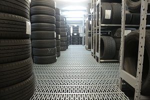 Rows of tires stacked in a storage room with metal shelving and grated flooring.