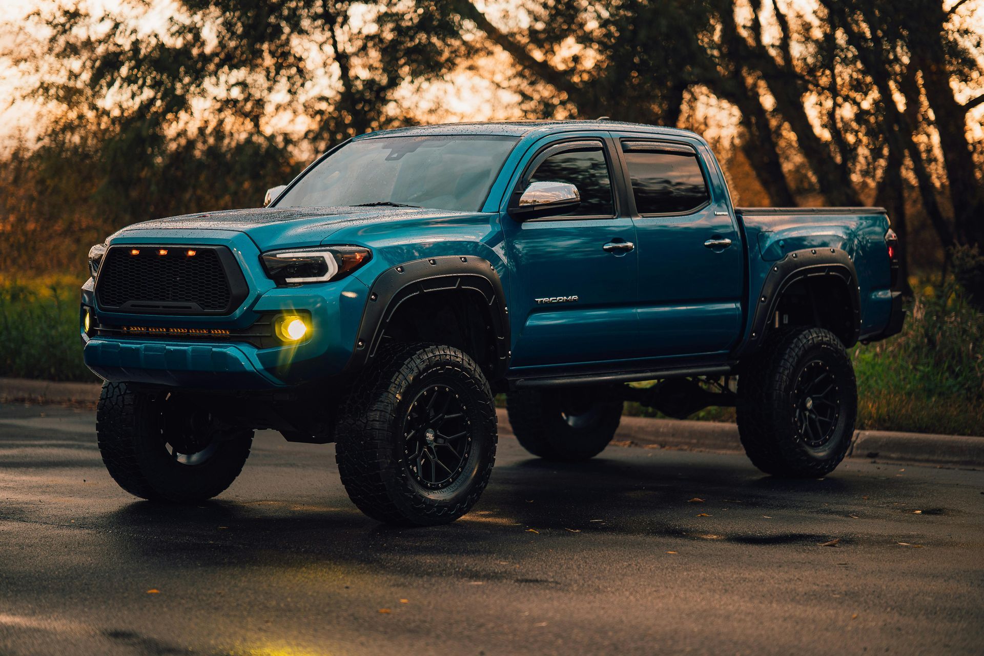 Teal lifted pickup truck with black wheels parked on wet pavement.