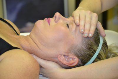 A woman is laying on a bed getting a head massage.