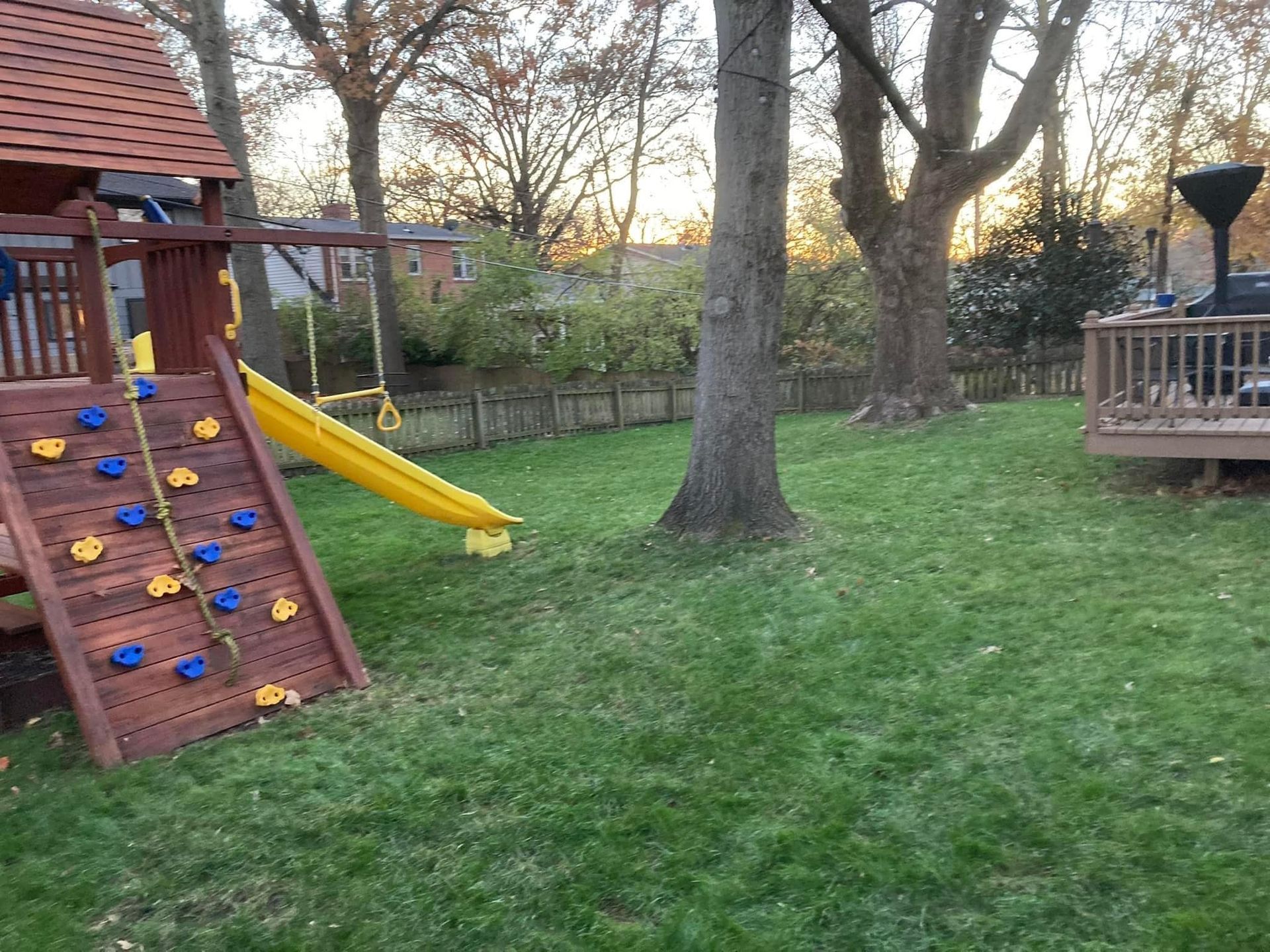 Backyard with a wooden playset, slide, climbing wall, swing, and a grassy lawn.