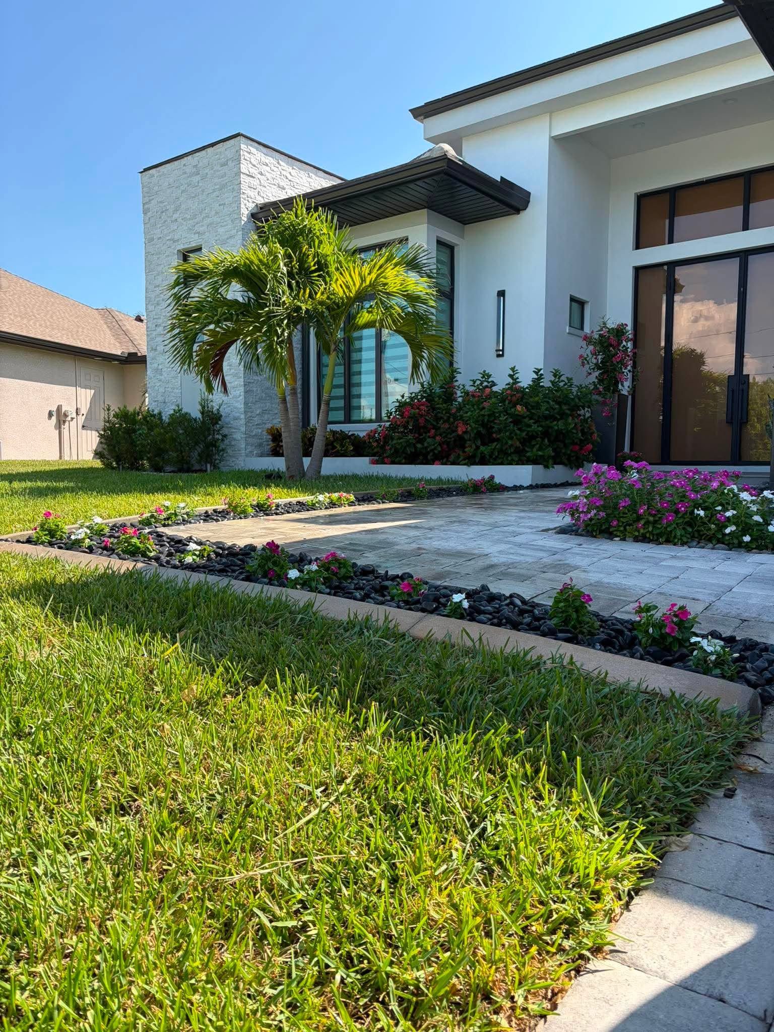 Modern white house with manicured lawn, flower beds, and palm trees in bright daylight