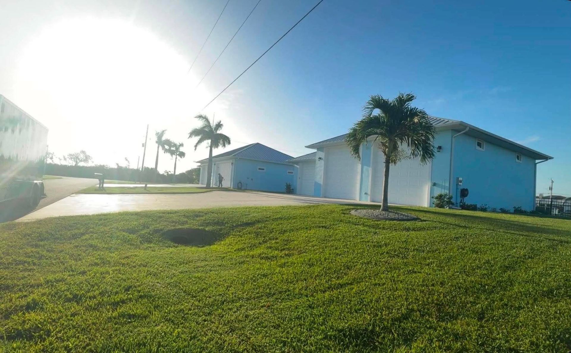 Sunlit suburban house with a large green lawn and palm trees under a bright sky