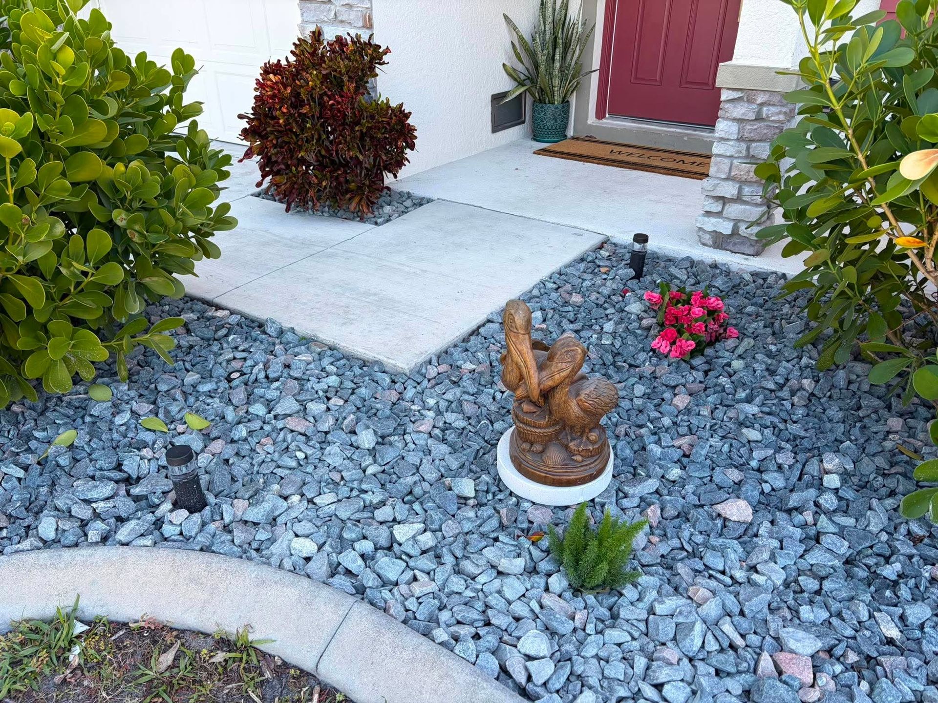 Front walkway with gray rocks, a small rabbit statue, red door, and potted plants by the entrance