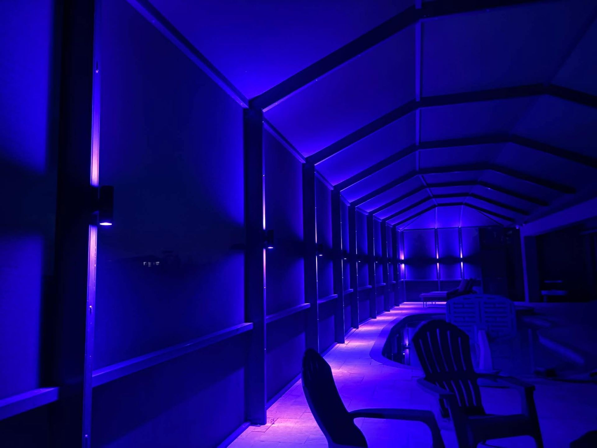 Blue-lit enclosed walkway with chairs along the side and a curved ceiling