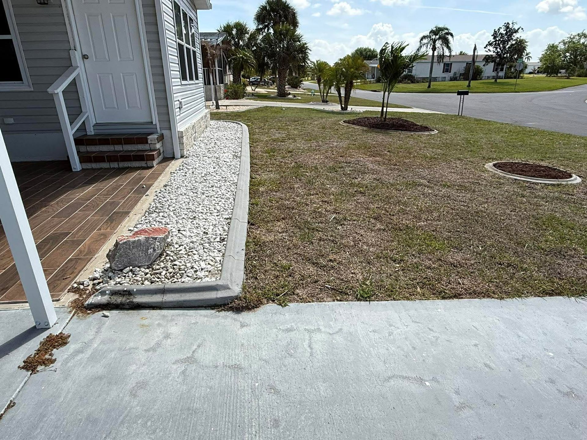 Front yard with a house porch, concrete driveway, and small trees in a grassy lawn.