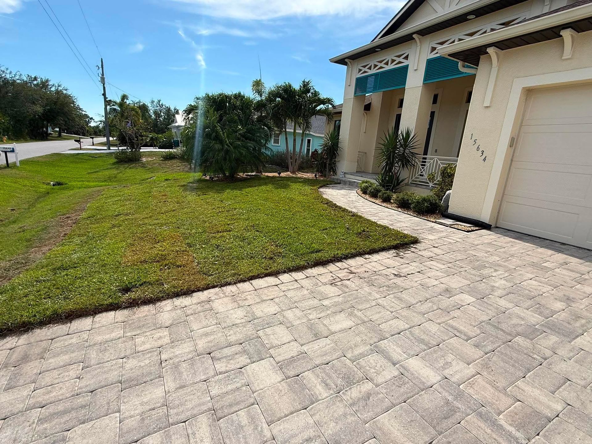Front yard with paved driveway, green lawn, and beige house with a garage under a blue sky.