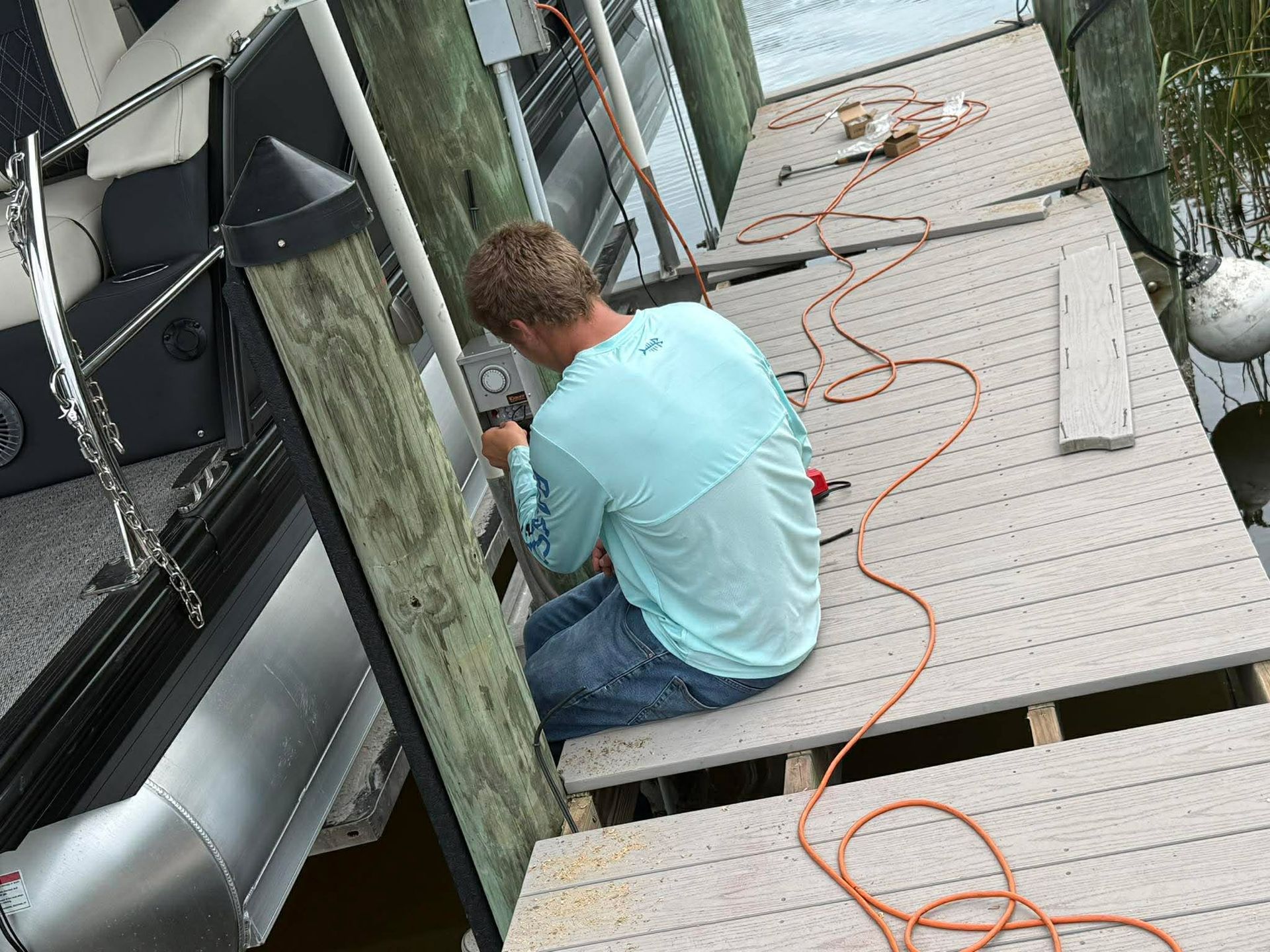 Person kneeling on a rooftop, using a tool near a wall with an orange extension cord nearby.