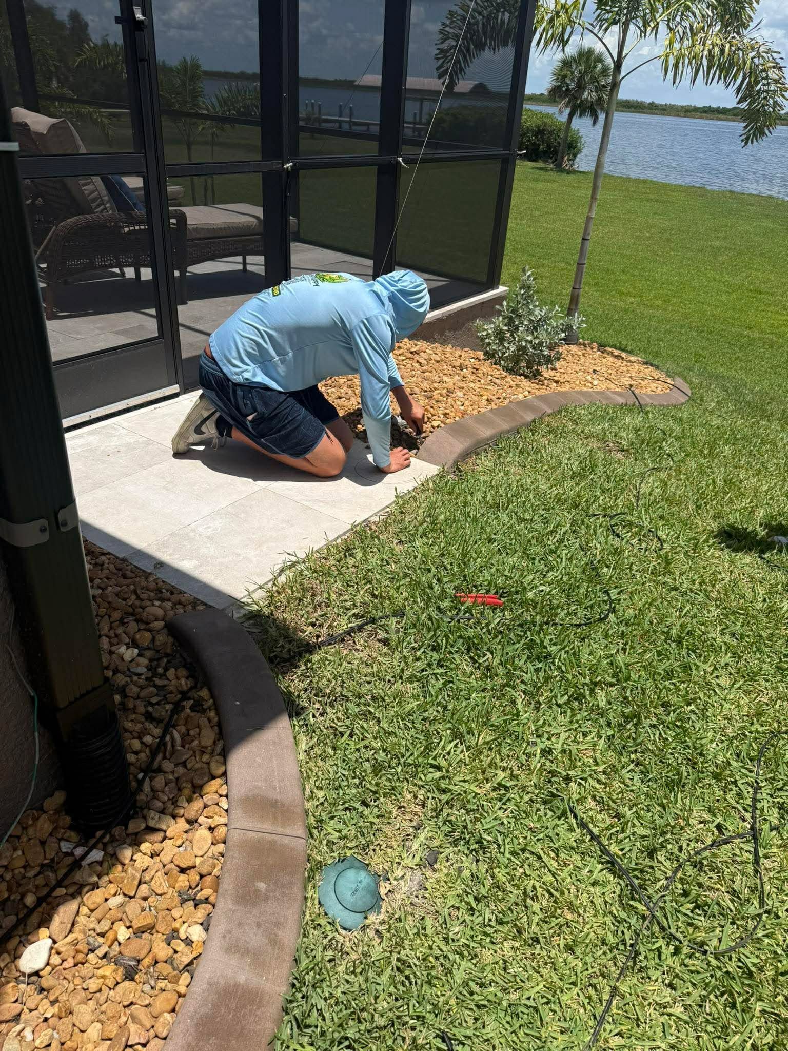 Person kneeling by a patio edge, digging or planting near a screened porch beside a lake.